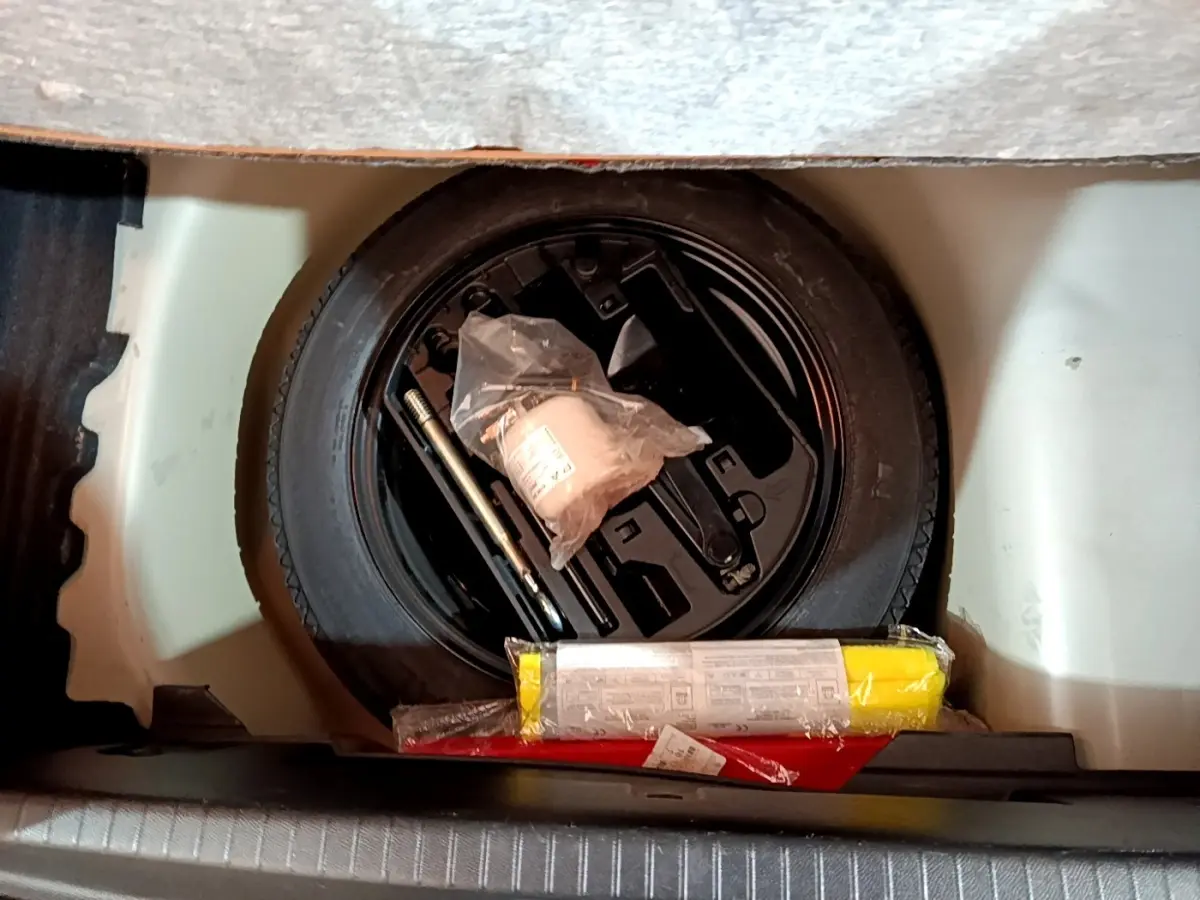 Vue plongeante sur la roue de secours noire et les outils de bord dans le coffre d'une Peugeot 208 blanche.
