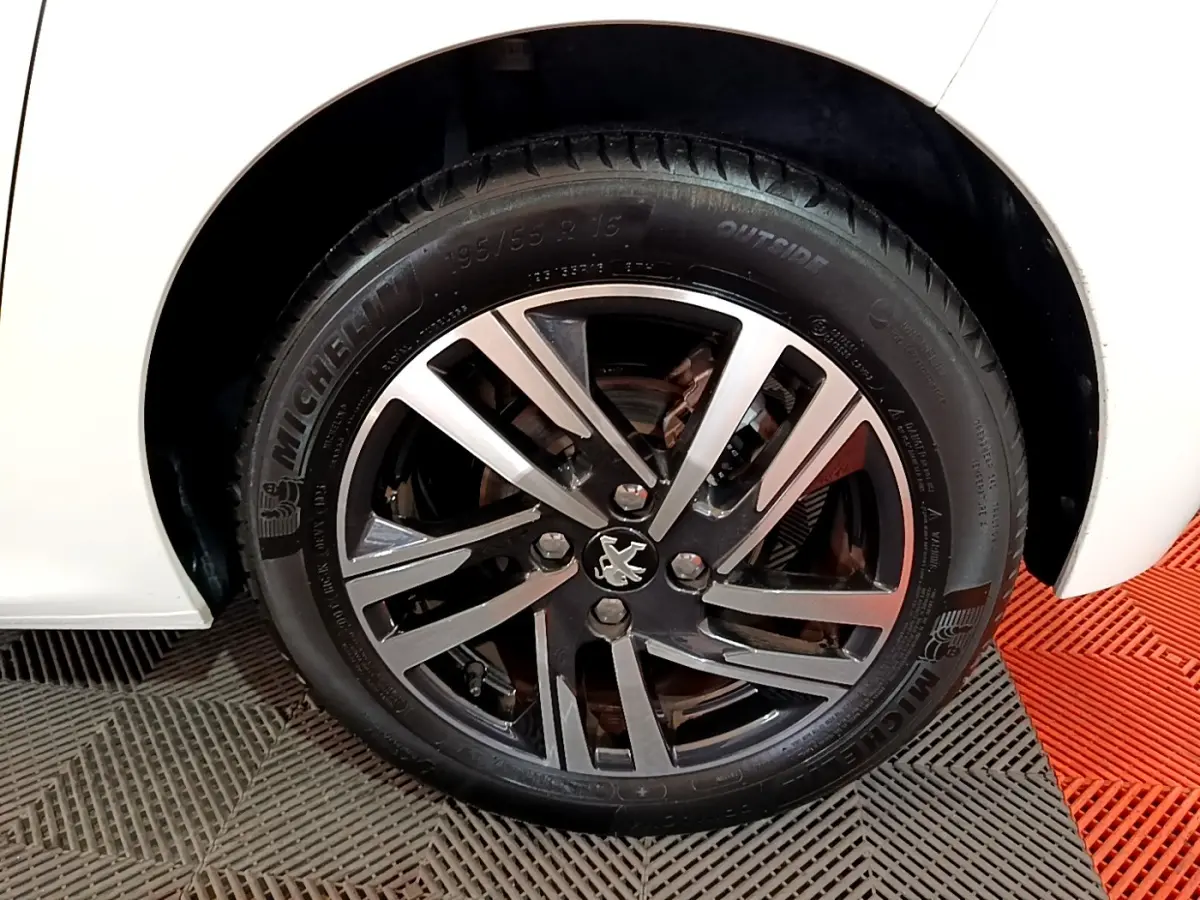 Gros plan sur la roue avant gauche blanche d'une Peugeot 208 avec jante alliage noire et argentée au logo lion.