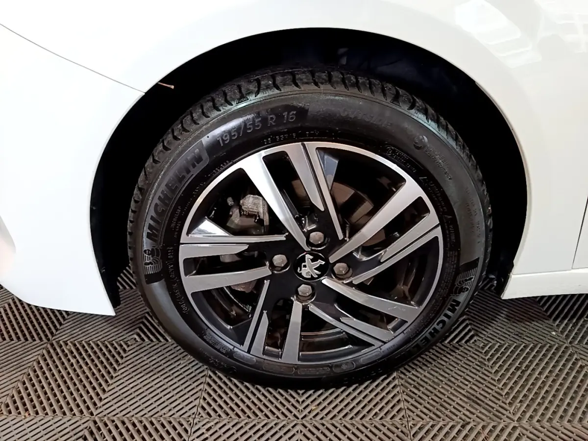 Gros plan sur la roue avant droite d'une Peugeot 208 blanche, jante alliage noire et argent avec logo lion central.