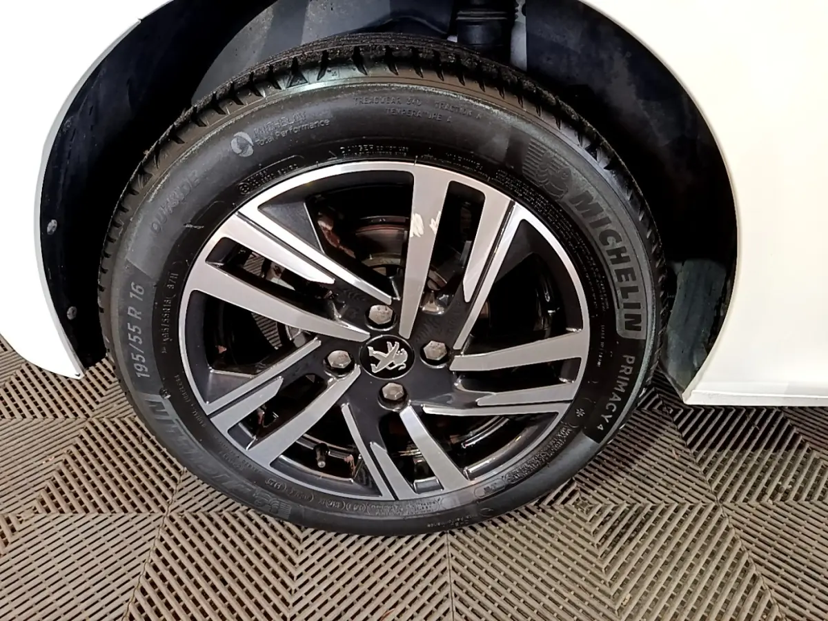 Gros plan sur la roue avant droite d'une Peugeot 208 blanche, jante alliage noire et argent avec logo lion central.