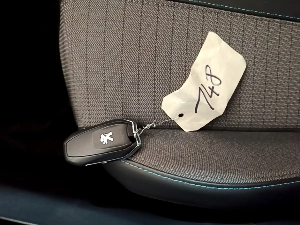 Clé de voiture Peugeot posée sur un siège tissu gris avec surpiqûres bleues, vue en gros plan intérieur.