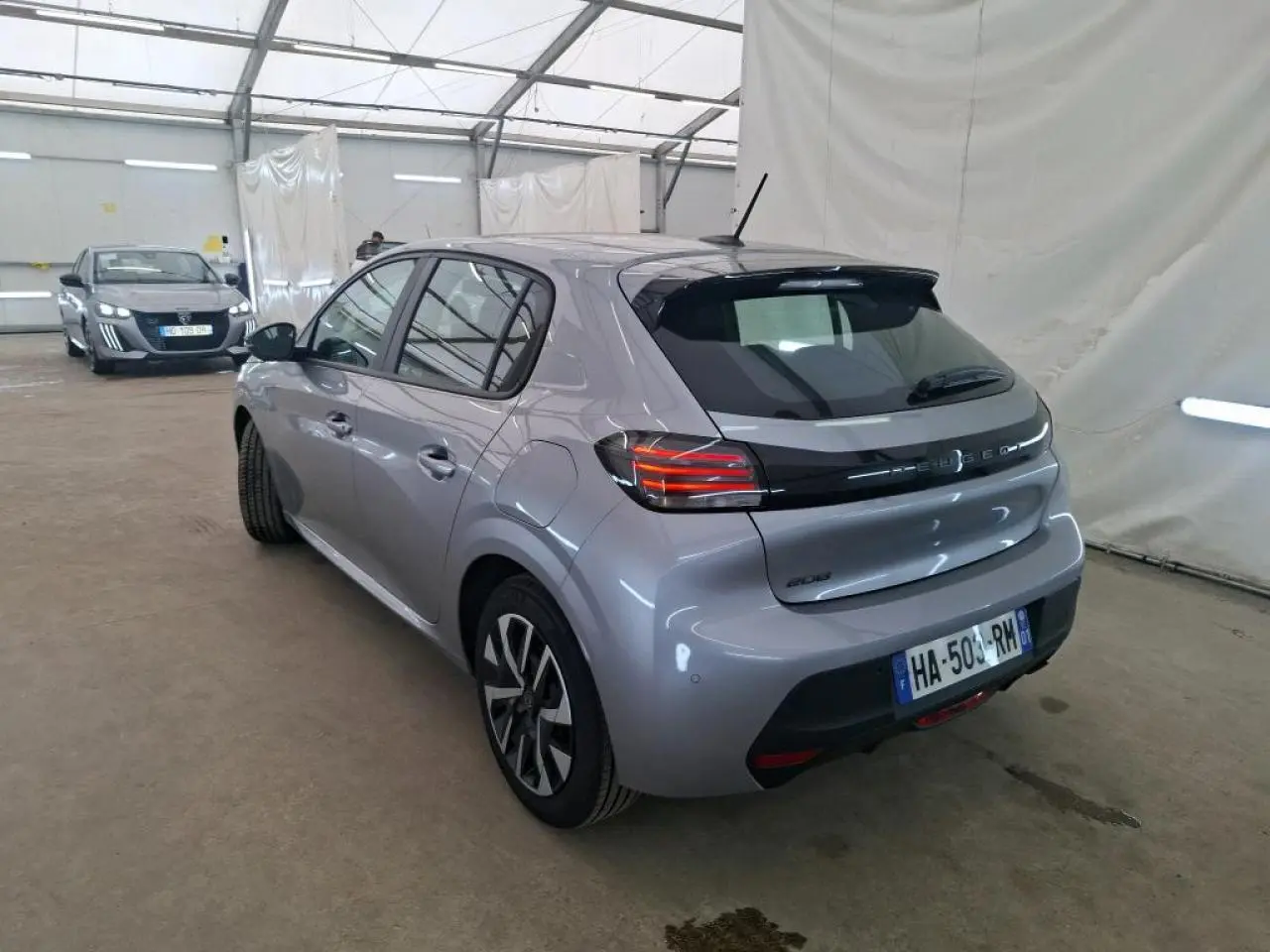 Vue 3/4 arrière droite d'une Peugeot 208 gris clair 2024, avec feux arrière LED et jantes alliage distinctives.