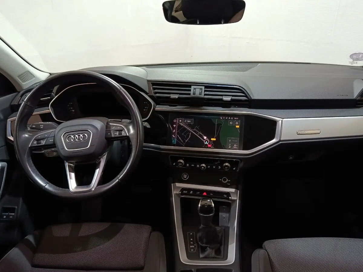 Vue intérieure avant de l'Audi Q3 Sportback gris foncé, mettant en valeur le volant cuir multifonctions et l'écran tactile central.