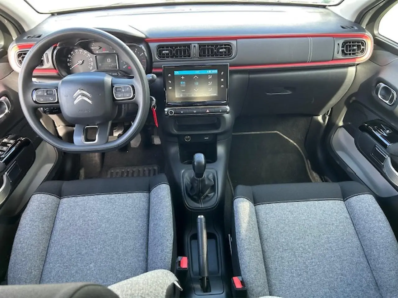 Vue intérieure avant de la Citroën C3 C-Series 2021, tableau de bord noir avec bande rouge et sièges gris bicolores.