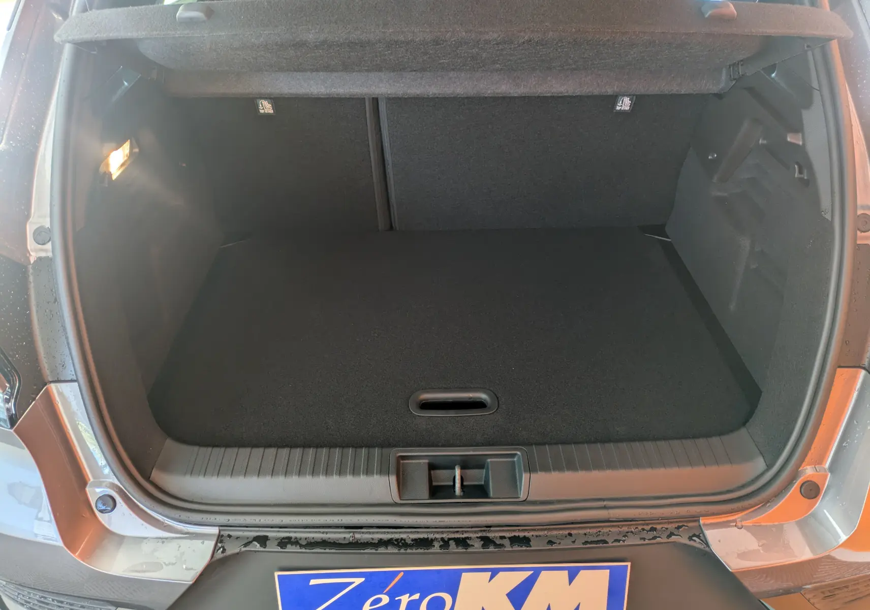 Coffre ouvert vu de l'arrière d'un Renault Captur E-Tech gris Cassiopée avec intérieur noir et seuil de chargement visible.