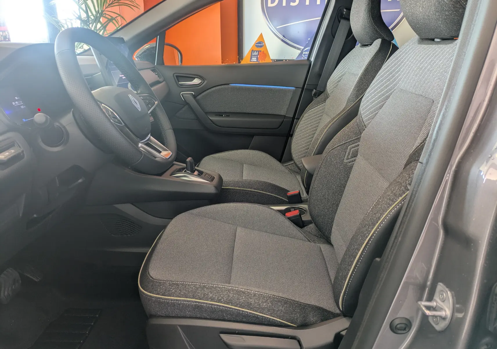 Intérieur avant droit du Renault Captur gris Cassiopée 2025, sièges tissu gris avec surpiqûres jaunes et volant multifonction.