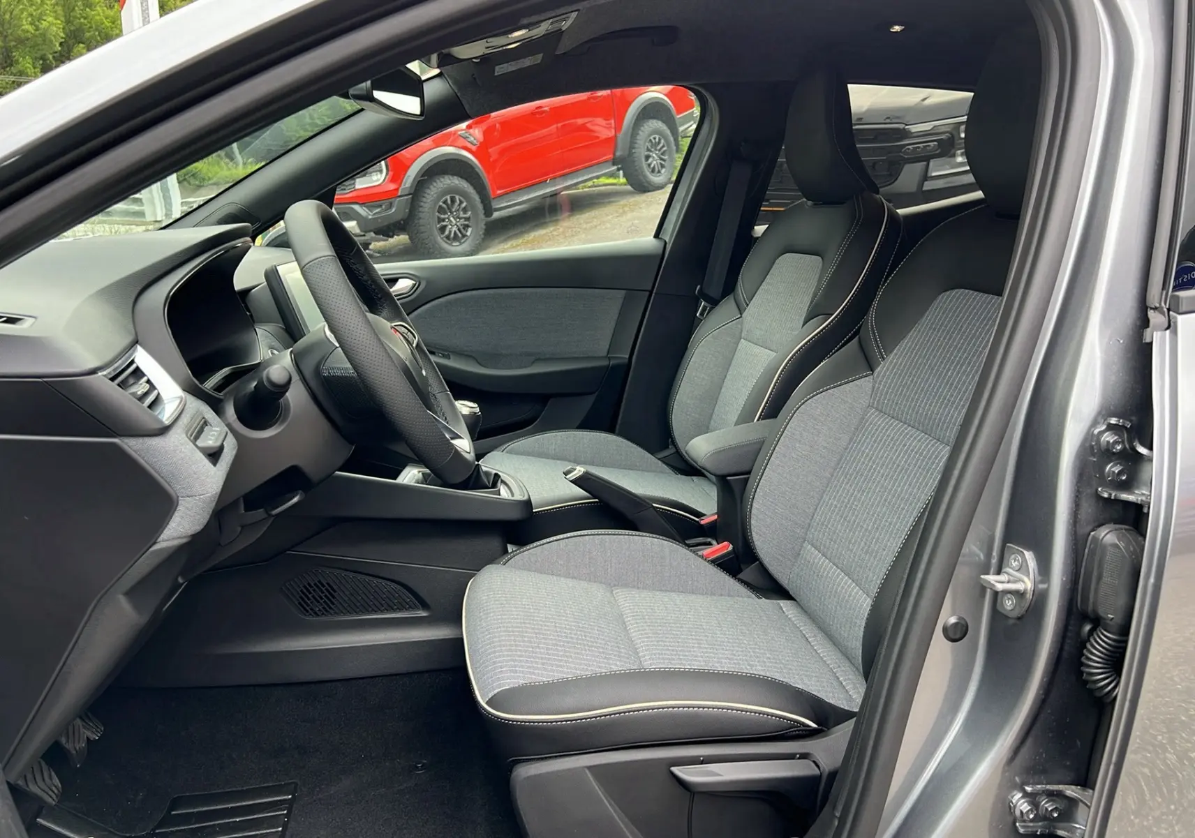 Intérieur de la Renault Clio V TCE 90 Techno 2025 en gris schiste, vue côté conducteur avec sièges tissu et volant noir.
