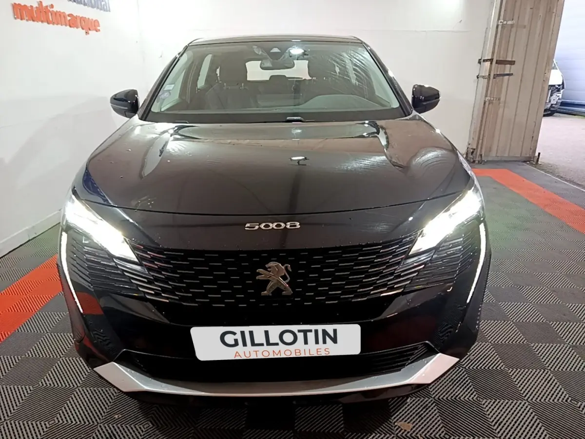 Vue avant d'un Peugeot 5008 noir 2021 avec phares LED allumés et calandre distinctive en concession.