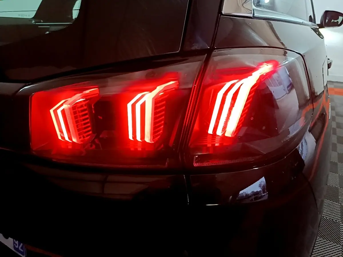 Gros plan sur le feu arrière droit rouge allumé d’un Peugeot 5008 noir, vue en légère plongée.