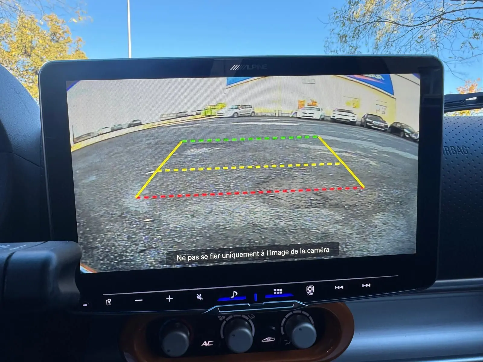 Écran de caméra de recul affichant une vue arrière avec lignes de guidage colorées, intérieur noir du tableau de bord.