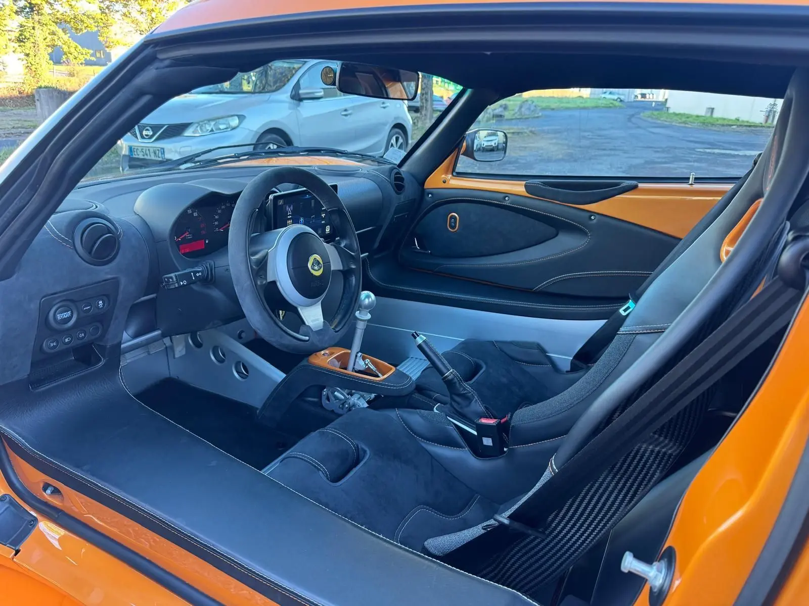 Vue intérieure côté conducteur de la Lotus Elise 3 Cup 250 orange, avec sièges sport en Alcantara noir et volant cuir.