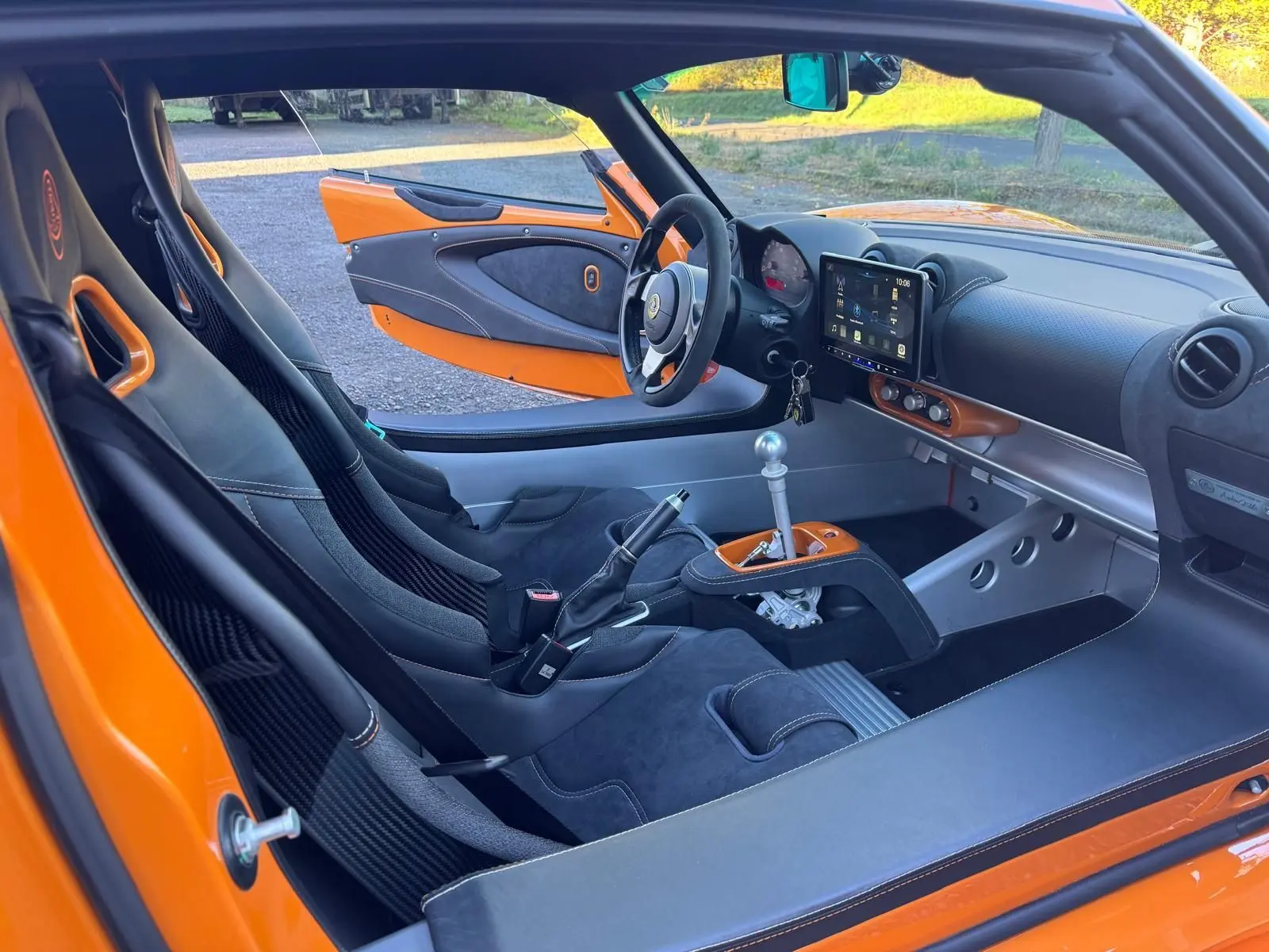 Vue intérieure côté conducteur de la Lotus Elise 3 Cup 250 orange, mettant en valeur les sièges sport en Alcantara noir et la console centrale avec levier de vitesses alu.