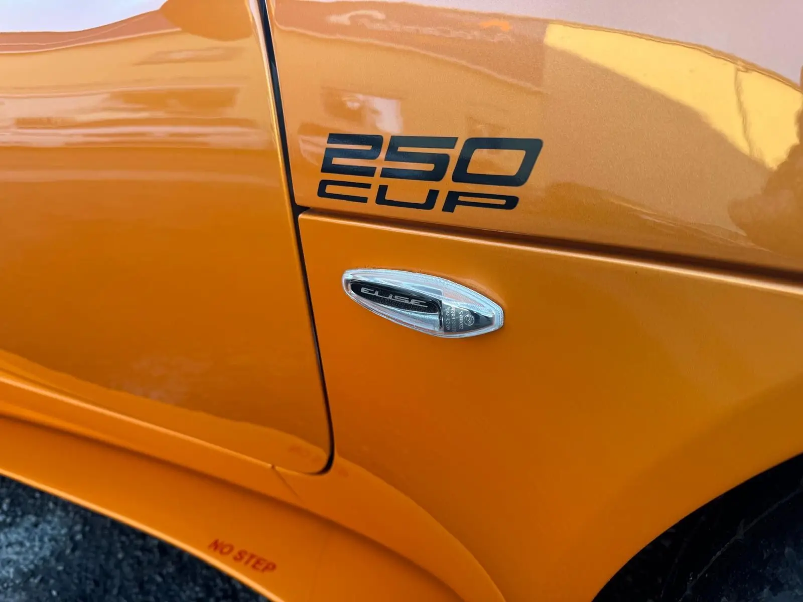 Gros plan sur l'aile avant droite orange de la Lotus Elise 3 Cup 250 avec logo "250 CUP" et répétiteur latéral.