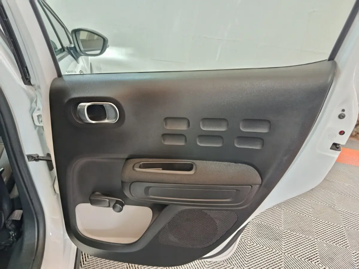 Vue intérieure de la porte arrière droite blanche d'une Citroën C3 2020 avec poignée chromée et manivelle de vitre.