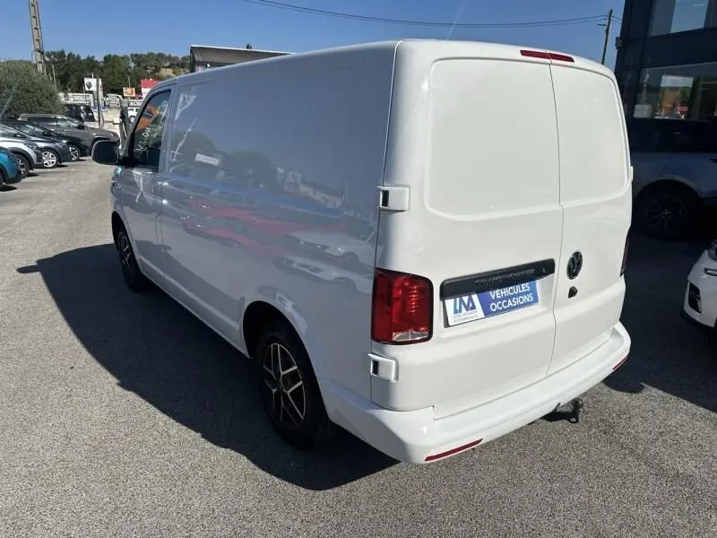 Vue 3/4 arrière droite d'un Volkswagen Transporter blanc 2022, fourgon utilitaire avec jantes noires et feux rouges.