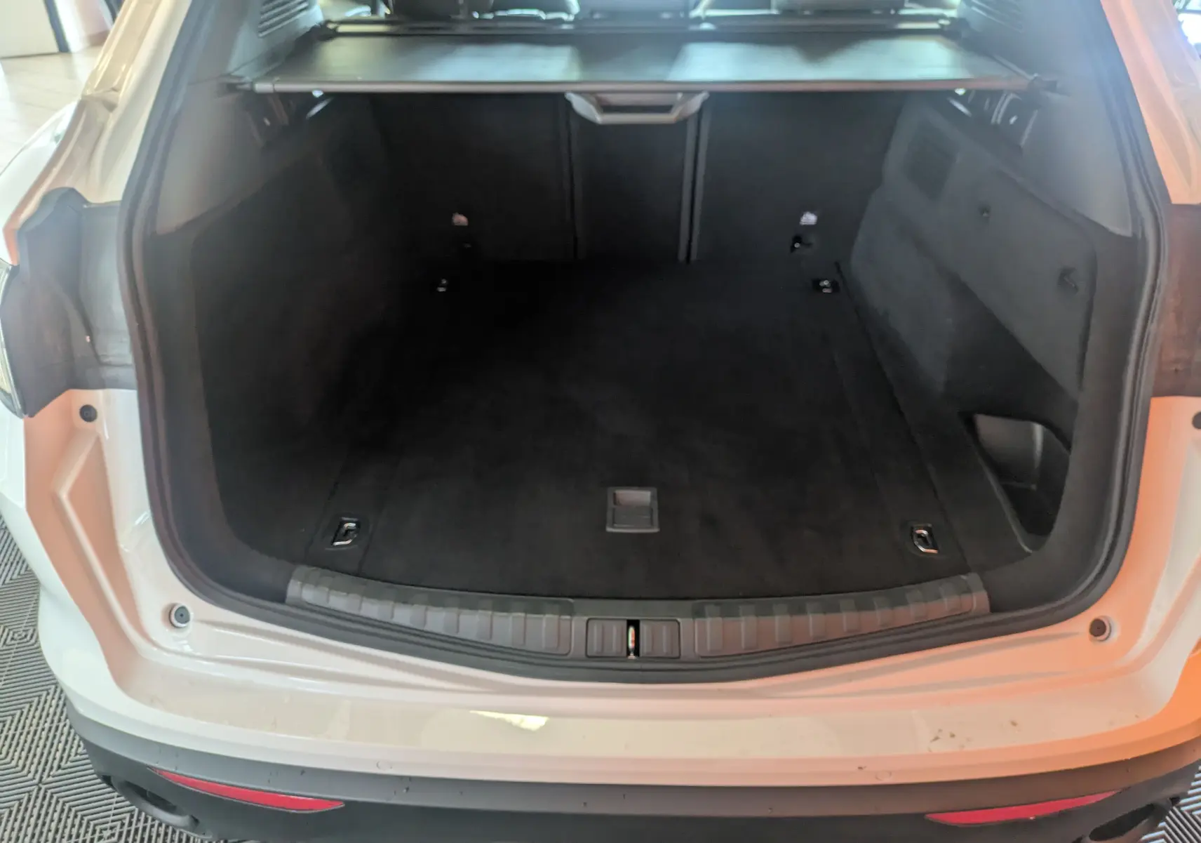 Coffre ouvert d'un Alfa Romeo Stelvio blanc 2023, vue arrière montrant l'espace de chargement noir et les sièges arrière.