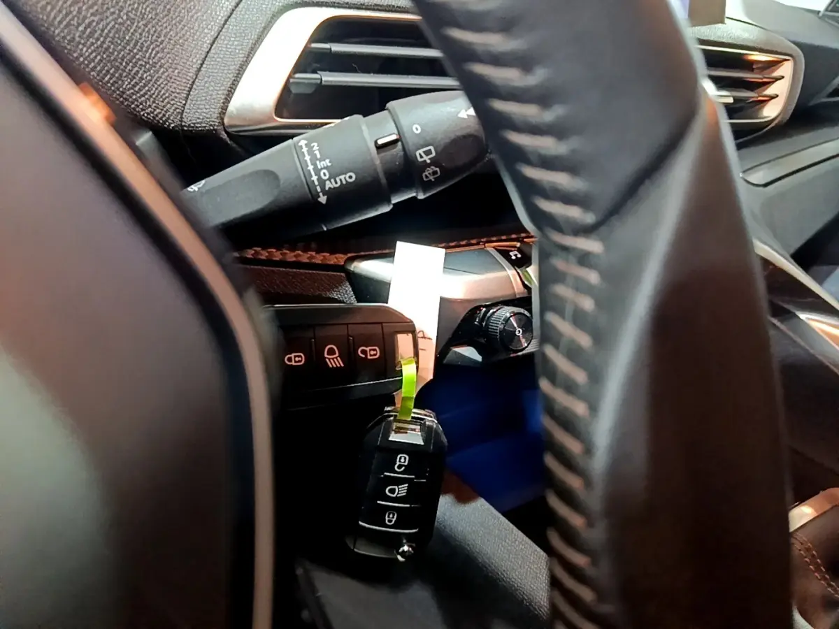 Gros plan intérieur côté conducteur du Peugeot 3008 gris clair, volant cuir et commandes de phares visibles.