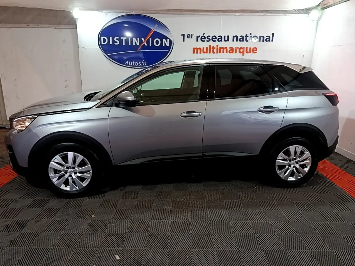 Vue latérale droite d'un Peugeot 3008 gris clair de 2020, avec jantes alliage et toit noir contrasté en intérieur showroom.