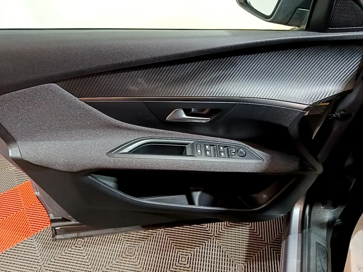 Vue rapprochée de la porte avant gauche grise du Peugeot 3008 avec commandes électriques et insert effet carbone.