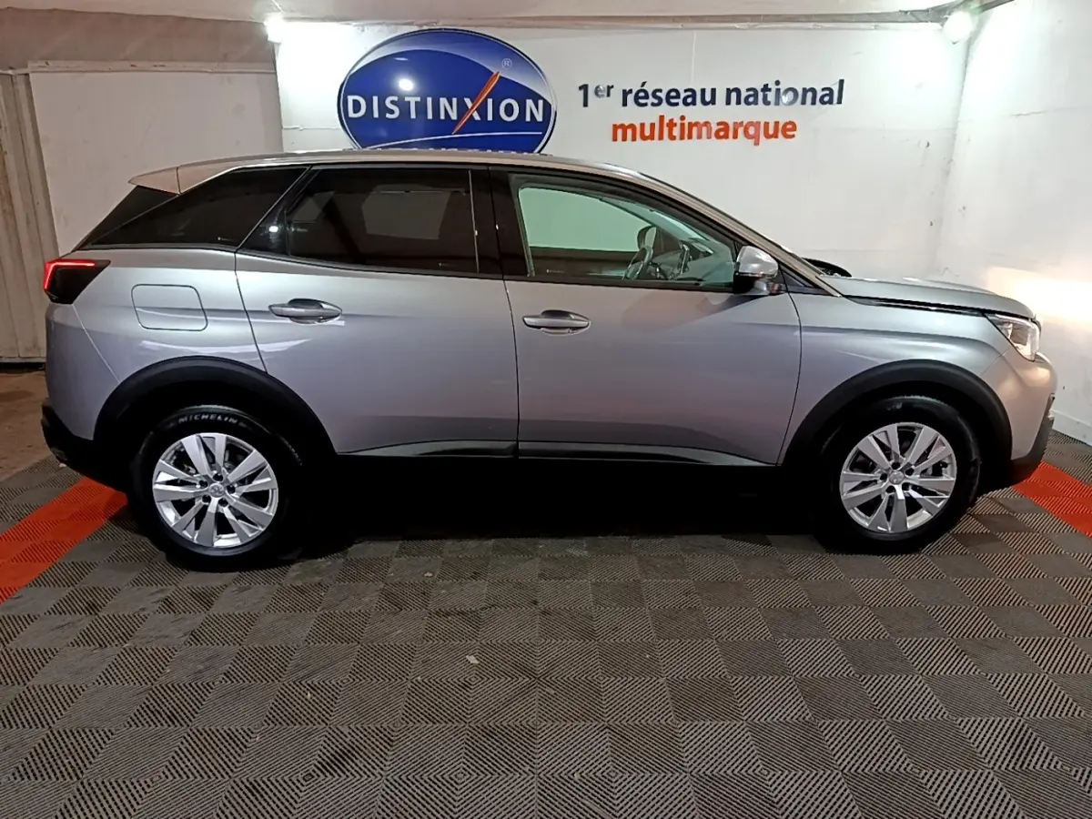 Vue de profil droit d’un Peugeot 3008 gris clair 2020 dans un showroom avec logo Distinxion en arrière-plan.