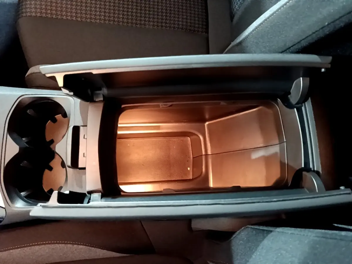 Vue plongeante sur le rangement central ouvert et porte-gobelets à l'intérieur du Peugeot 3008 gris clair de 2020.