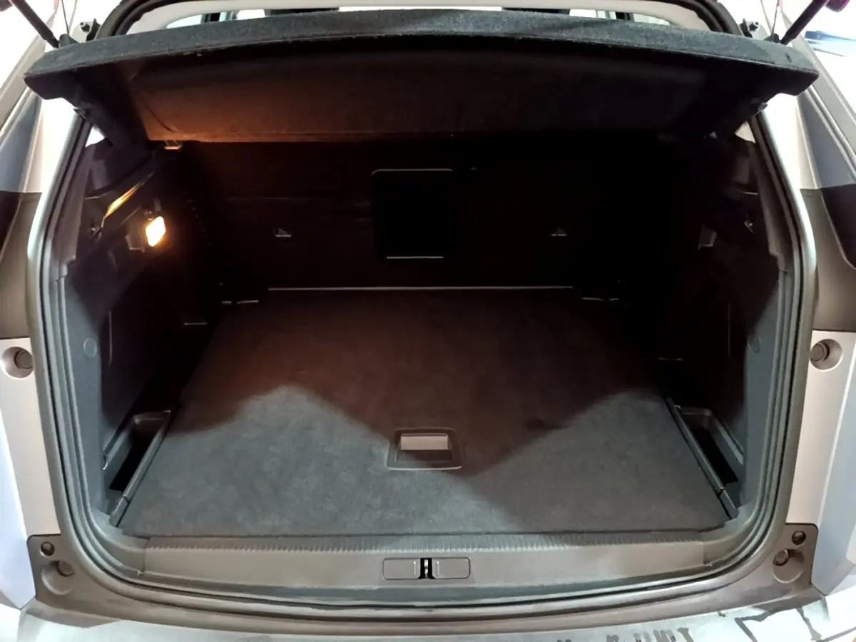 Coffre ouvert vu de l'arrière d'un Peugeot 3008 gris clair, espace de chargement propre et éclairé à gauche.