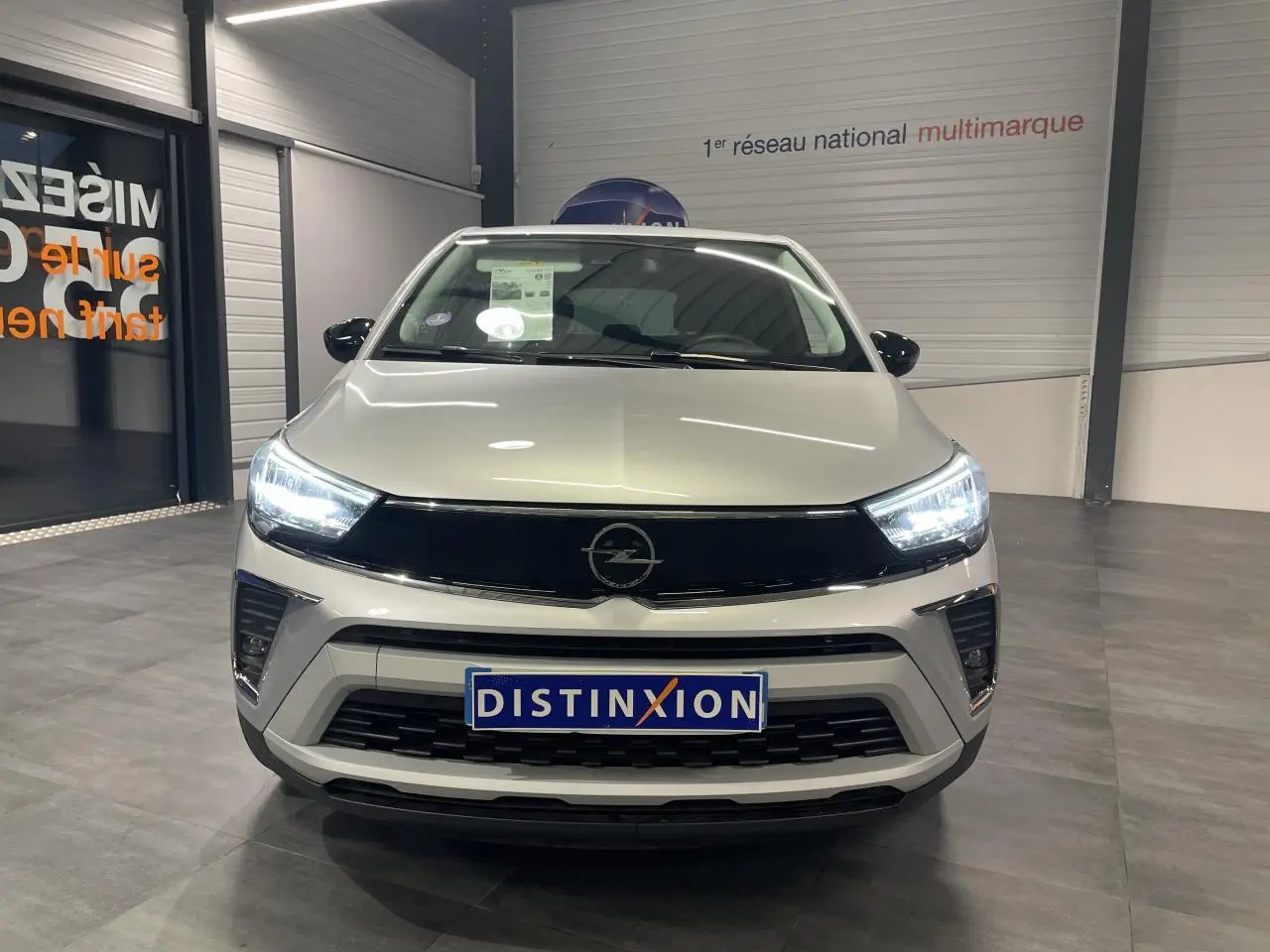 Vue frontale d'un Opel Crossland gris clair 2024 avec phares LED allumés dans un showroom.