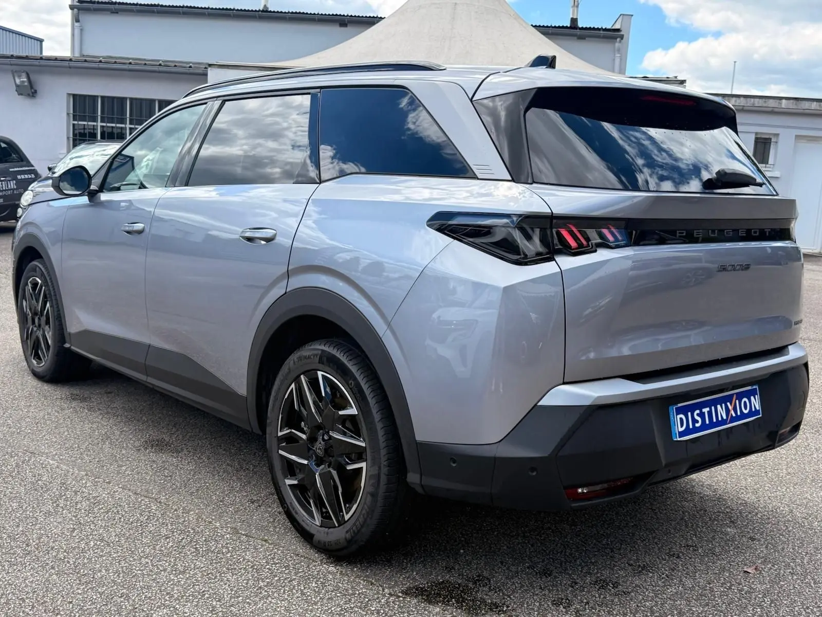 Vue 3/4 arrière droite du Peugeot 5008 Hybrid 145 gris Artense avec vitres teintées et jantes noires distinctives.
