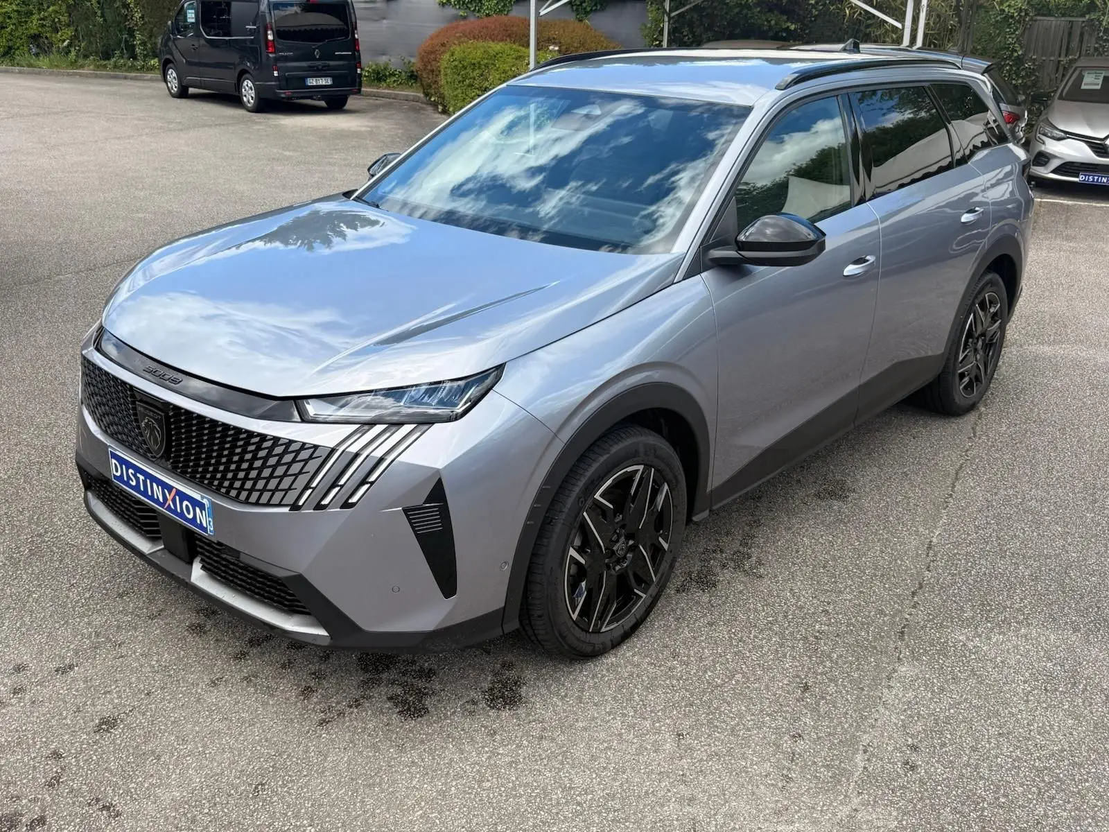 Peugeot 5008 Hybrid gris Artense vue 3/4 avant droit, avec calandre distinctive et jantes noires stylisées.