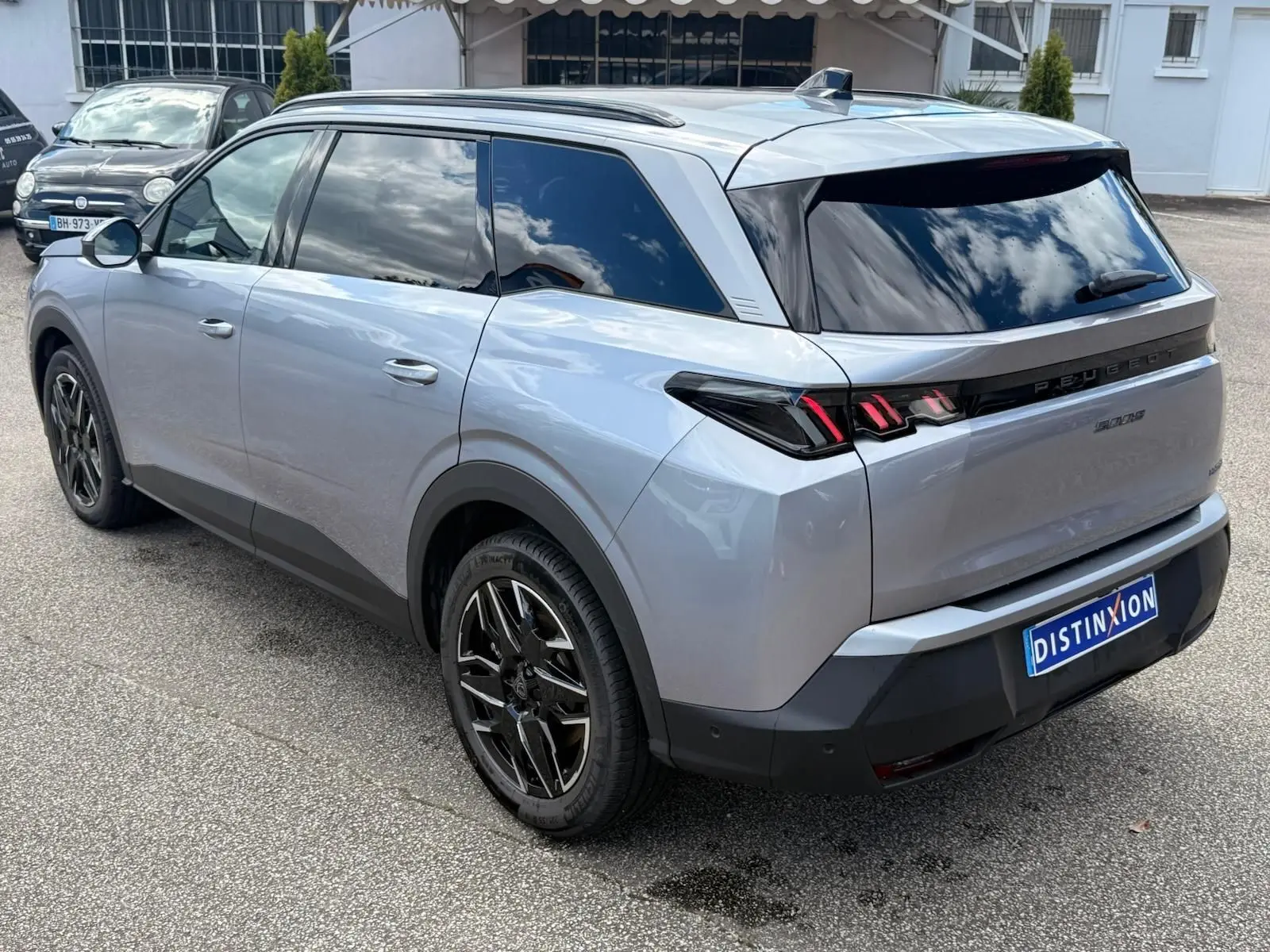 Peugeot 5008 Hybrid gris Artense vue 3/4 arrière droit, avec vitres teintées et jantes noires distinctives.