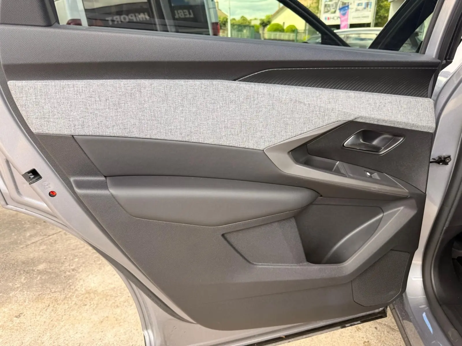 Vue intérieure du côté gauche de la porte arrière d’un Peugeot 5008 gris Artense, avec habillage tissu clair et plastique noir.