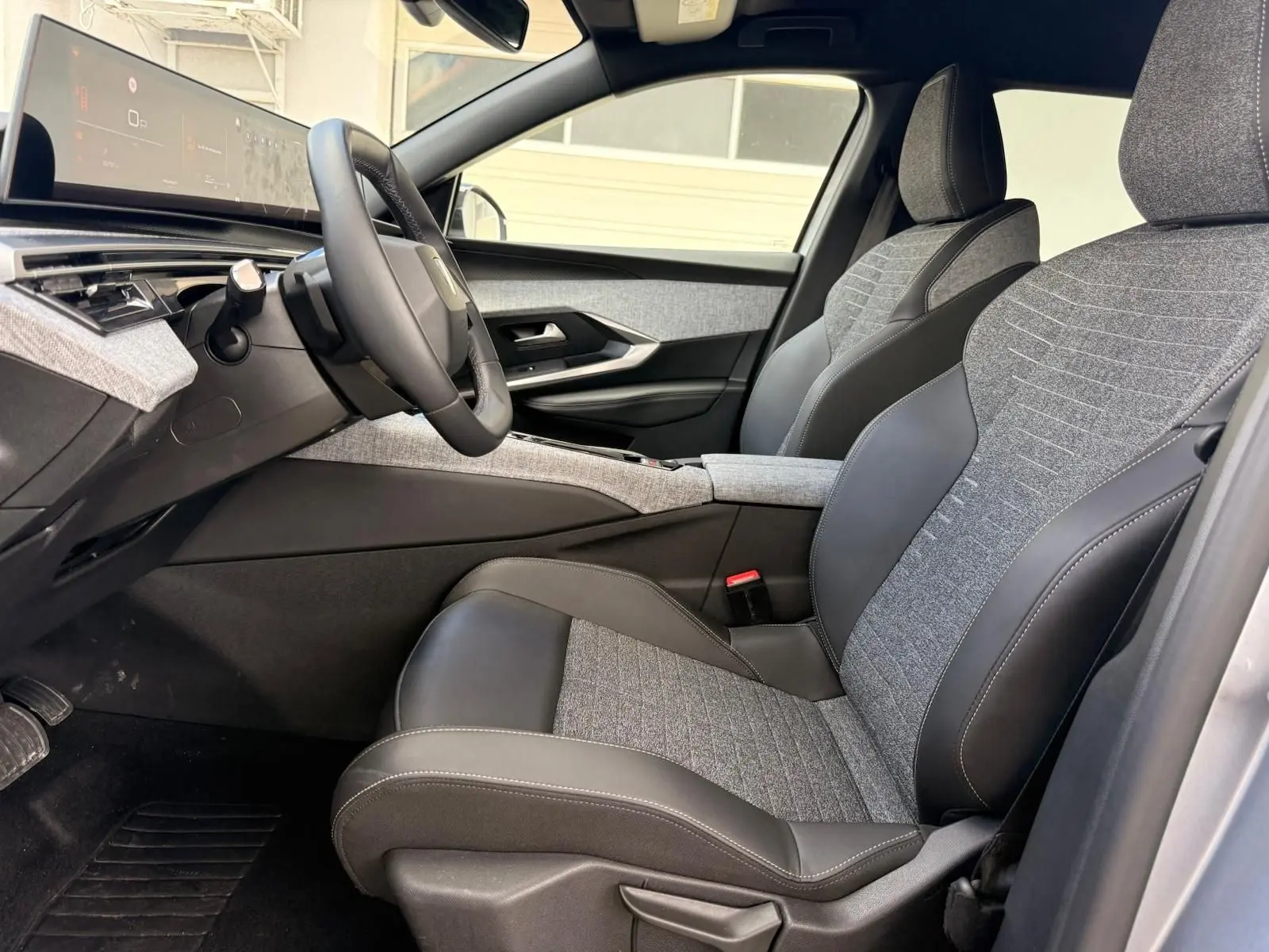 Vue intérieure côté conducteur du Peugeot 5008 Hybrid 145 en gris Artense, sièges tissu et cuir bicolores avec tableau de bord numérique.