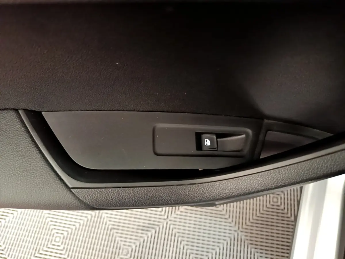 Gros plan sur le bouton de verrouillage des portes sur la portière intérieure noire d’un Skoda Karoq gris clair.