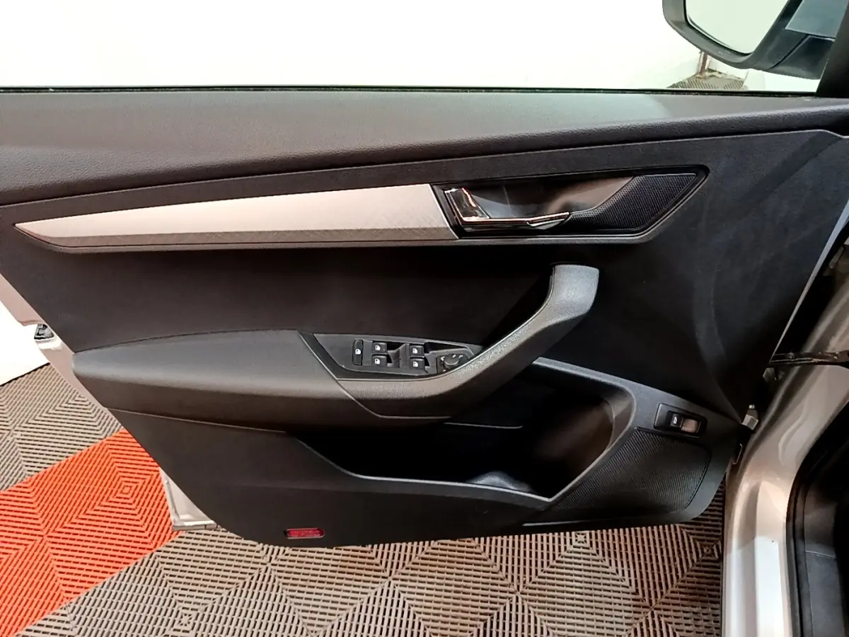 Vue intérieure côté gauche de la porte avant gris clair du Skoda Karoq avec commandes des vitres et poignée intégrée.