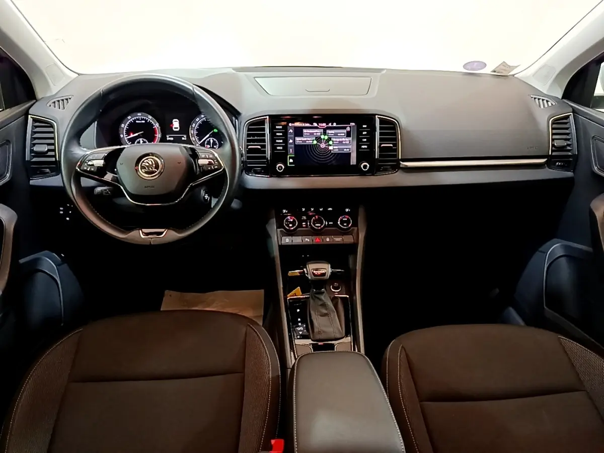 Vue intérieure frontale du tableau de bord et volant cuir noir du Skoda Karoq 1.5 TSI avec écran tactile central allumé.