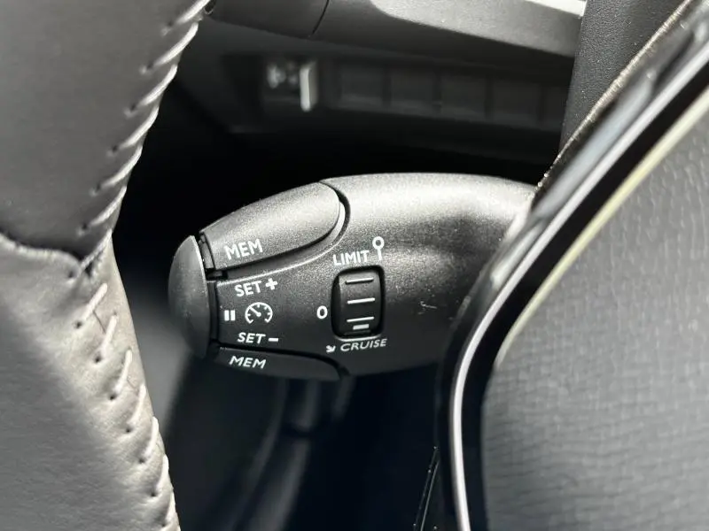 Gros plan sur la commande de régulateur de vitesse et limiteur sur le volant d'une Peugeot 208 2024.
