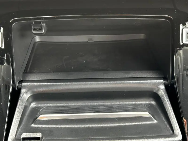 Gros plan sur la boîte à gants noire ouverte de la Peugeot 208 1.2 PureTech 100ch Allure 2024, intérieur épuré.