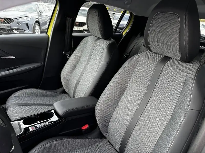 Intérieur avant de la Peugeot 208 1.2 PureTech 100ch Allure 2024, sièges tissu gris avec surpiqûres et accoudoir central noir.
