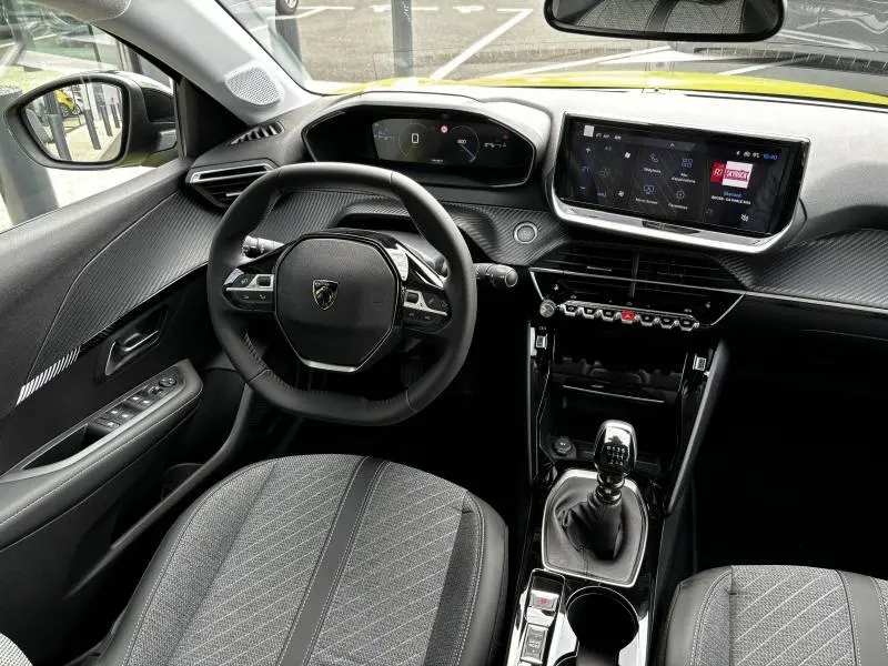 Vue intérieure avant de la Peugeot 208 1.2 PureTech 2024, tableau de bord noir avec écran tactile et volant compact.