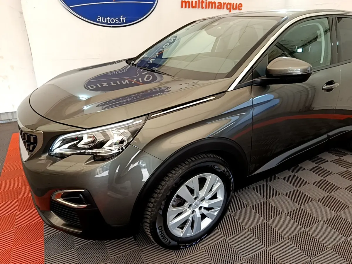 Peugeot 3008 gris foncé vue 3/4 avant droit, avec phares LED et jantes alliage visibles en intérieur showroom.