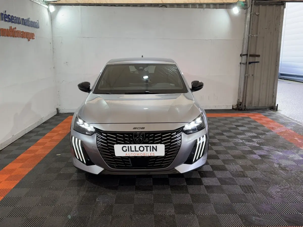 Vue frontale d'une Peugeot 208 Hybrid 136 eDCS6 GT gris clair avec phares LED et calandre noire distinctive.