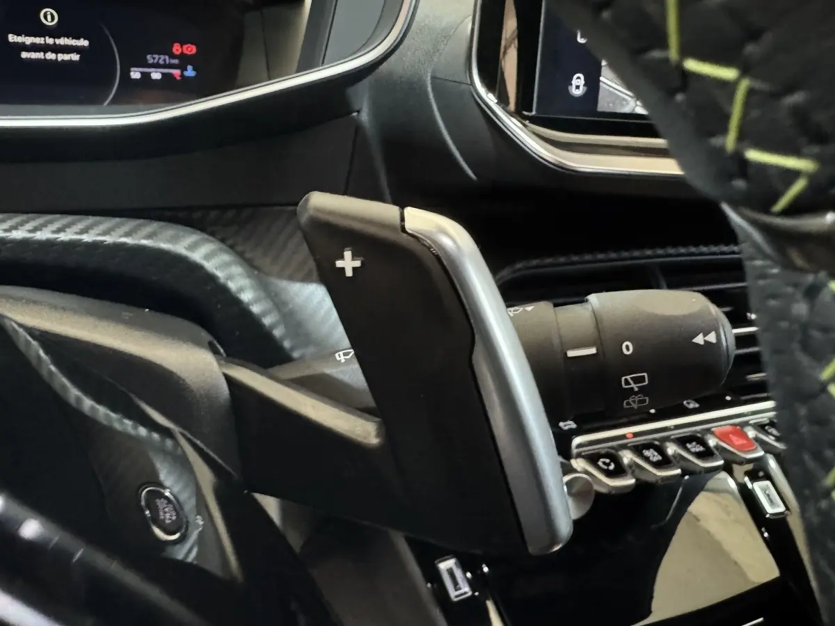 Gros plan sur la palette de changement de vitesse + côté droit du volant cuir avec surpiqûres vertes dans un Peugeot 208 gris clair.