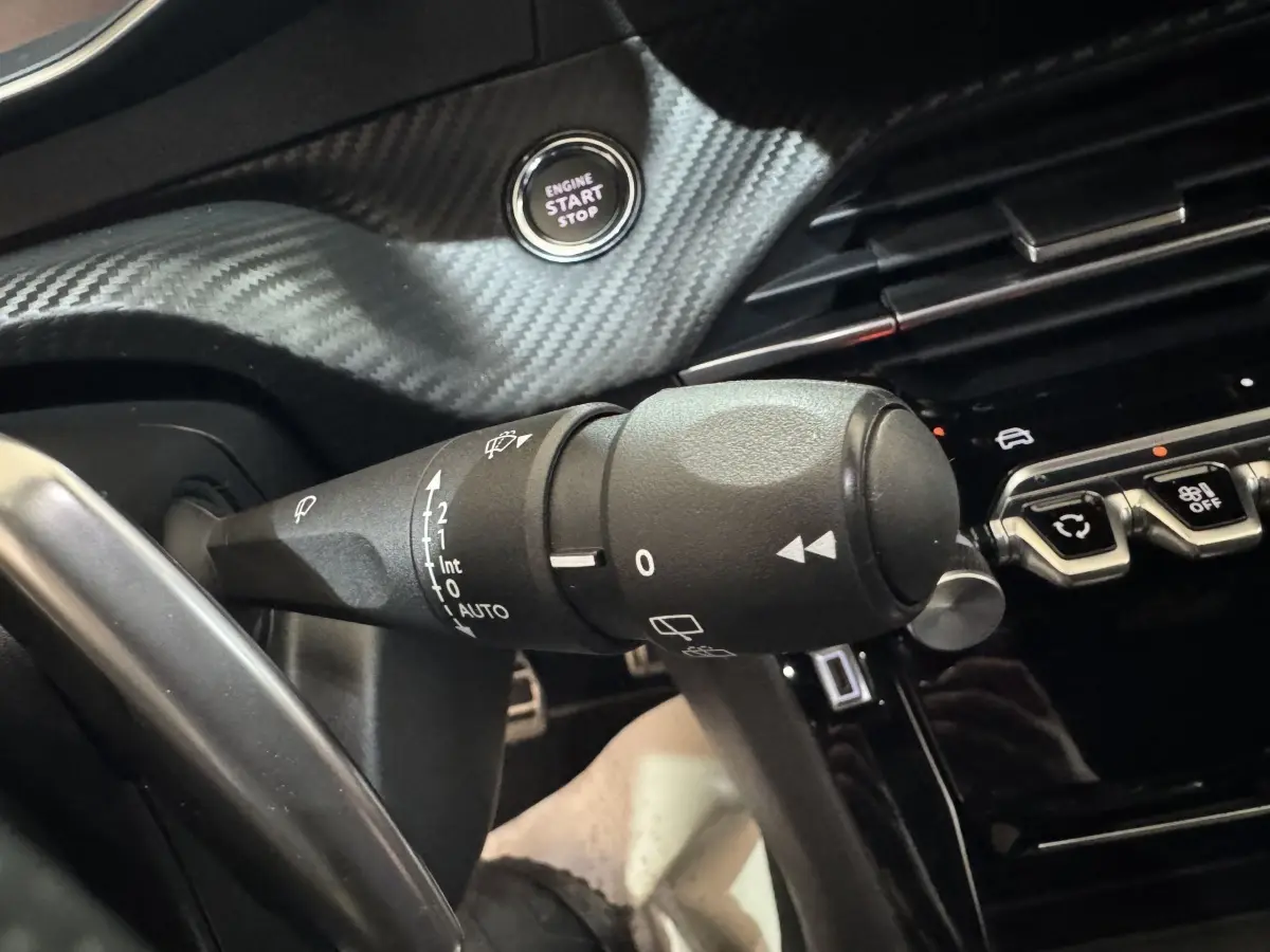 Gros plan sur la commande d’essuie-glace et bouton start/stop dans l’habitacle noir du Peugeot 208 Hybrid 136 eDCS6 GT.