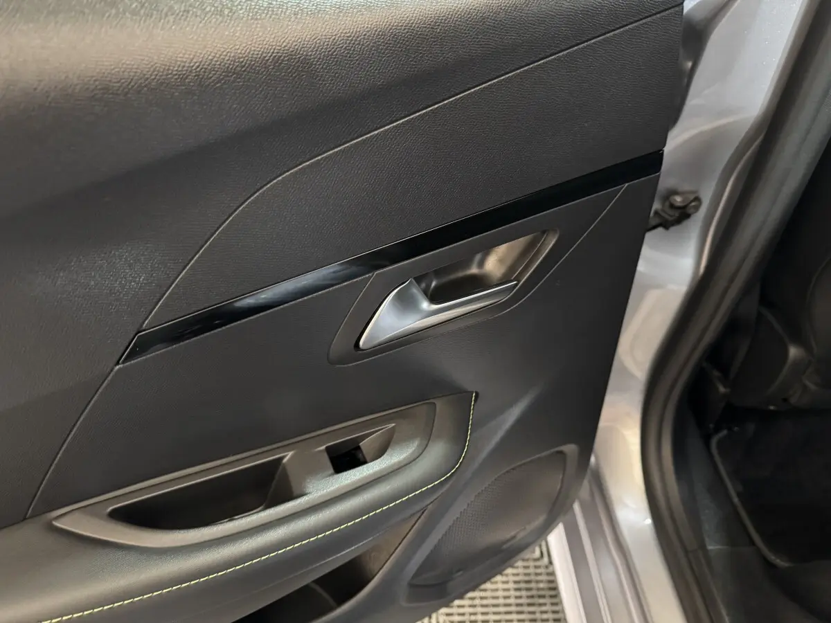 Gros plan sur la porte arrière droite intérieure noire avec surpiqûres vertes et poignée argentée d’une Peugeot 208 gris clair.