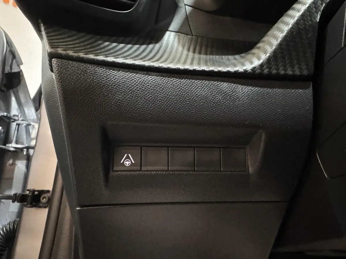 Gros plan sur les commandes latérales noires du tableau de bord d'une Peugeot 208 Hybrid gris clair, côté conducteur.