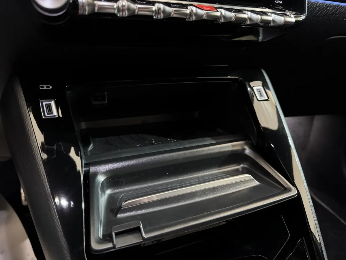 Détail de la console centrale noire de la Peugeot 208 Hybrid 136 eDCS6 GT avec ports USB et rangement ouvert.
