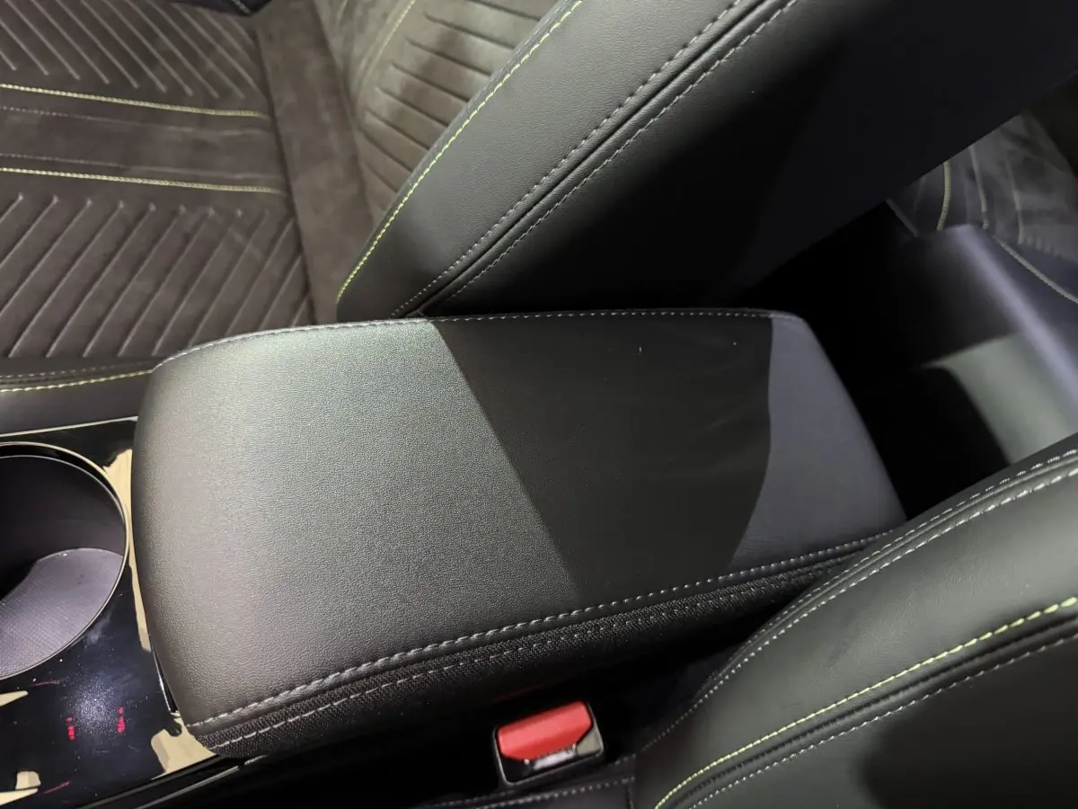 Gros plan sur l'accoudoir central en cuir noir avec surpiqûres vertes, sièges en tissu gris foncé à coutures vertes.