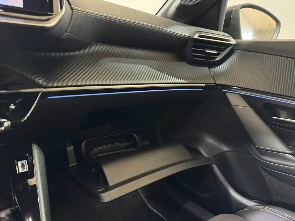 Intérieur côté passager de la Peugeot 208 Hybrid gris clair, tableau de bord avec finition carbone et éclairage d'ambiance bleu.