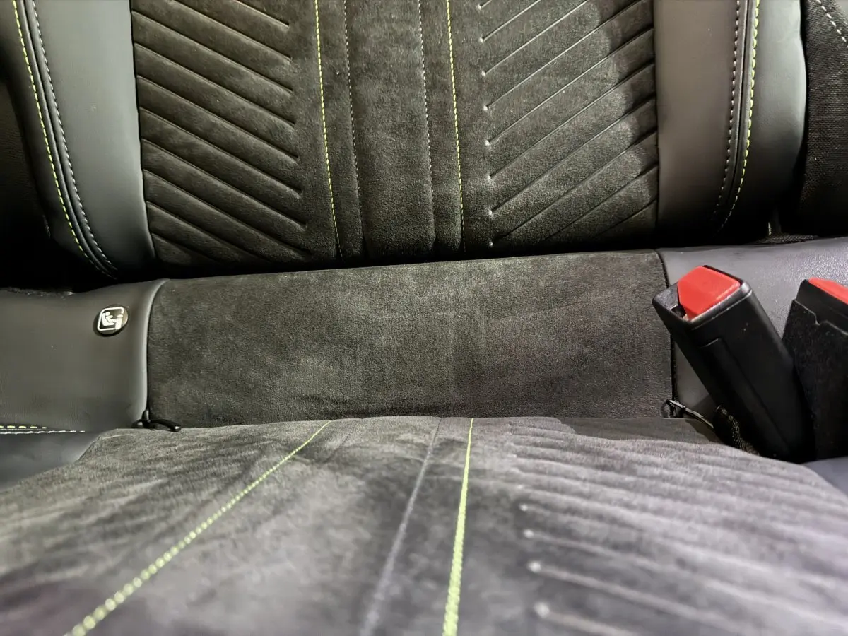 Gros plan sur la banquette arrière grise de la Peugeot 208 Hybrid 136 eDCS6 GT avec surpiqûres vertes et ceintures rouges.