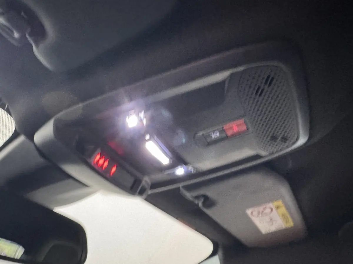 Vue intérieure du plafond avant de la Peugeot 208 Hybrid gris clair, montrant les éclairages et commandes intégrés.